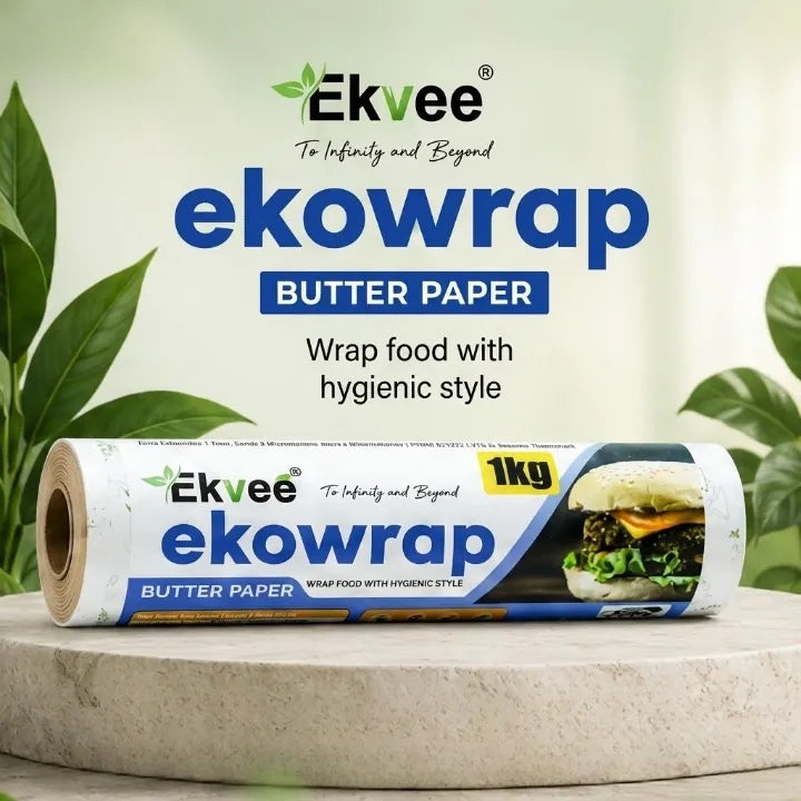 A 1kg roll of Ekvee Ekowrap Butter Paper is displayed on a light stone pedestal. The background is a soft, out-of-focus green with decorative leaves, and the product packaging is clearly visible with its branding and food usage example.