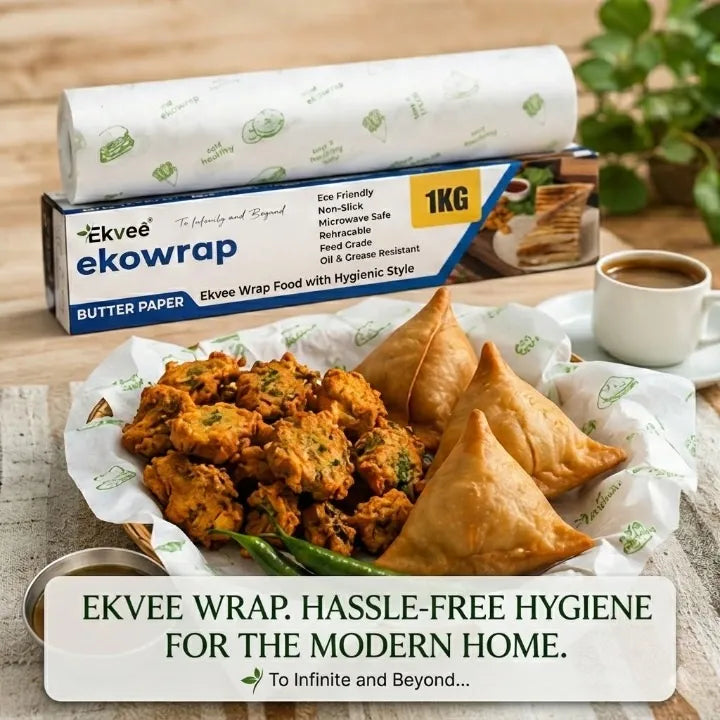 Ekvee Ekowrap 1KG Butter Paper food wrap box shown with a roll of white paper wrap and several fried samosas and pakoras on paper wrap, styled on a table with a cup of coffee and green leaves in the background.