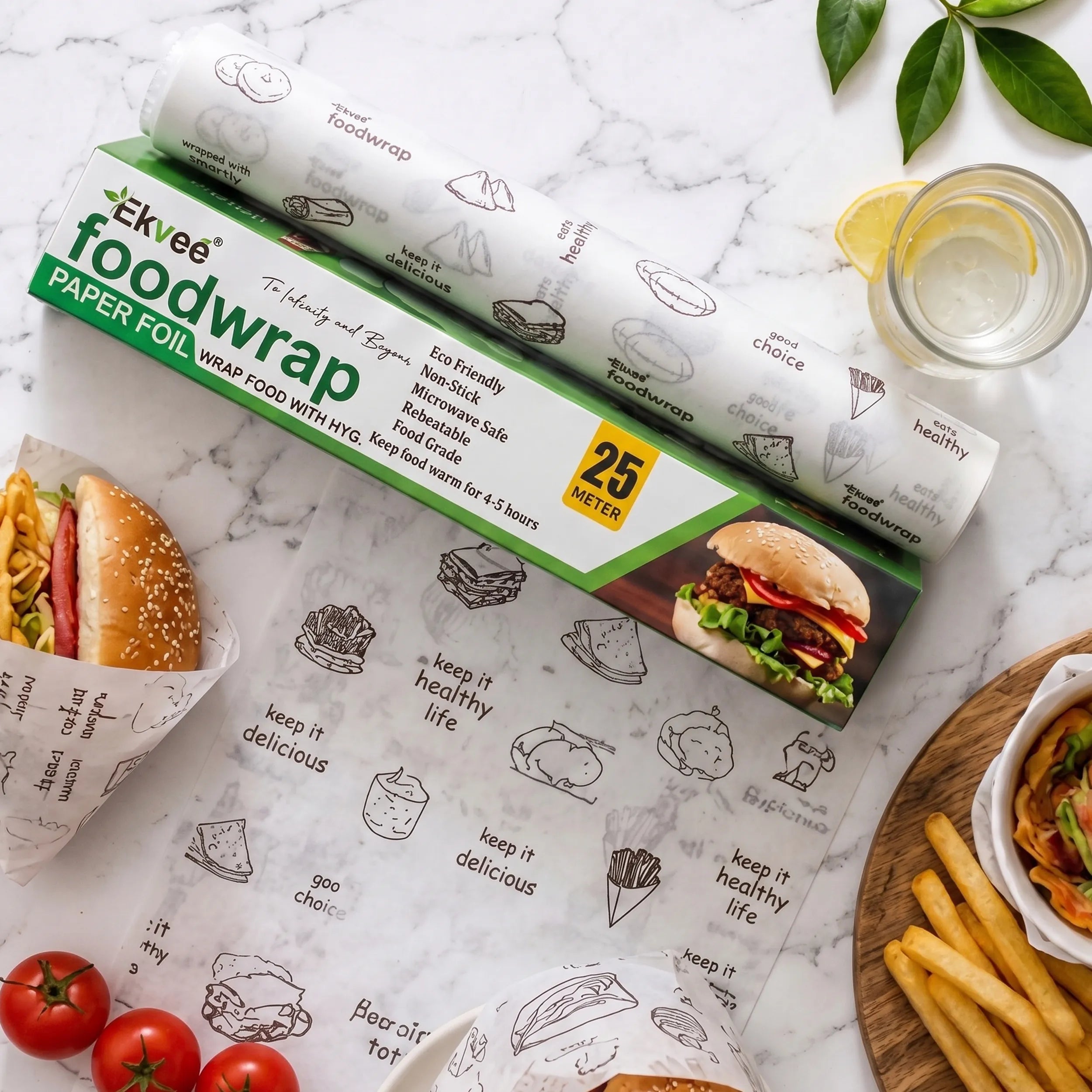 Ekvee paper food wrap roll and unrolled sheets on a white marble surface, styled with food props including a burger, fries, tomatoes, a lemon drink, and green leaves.