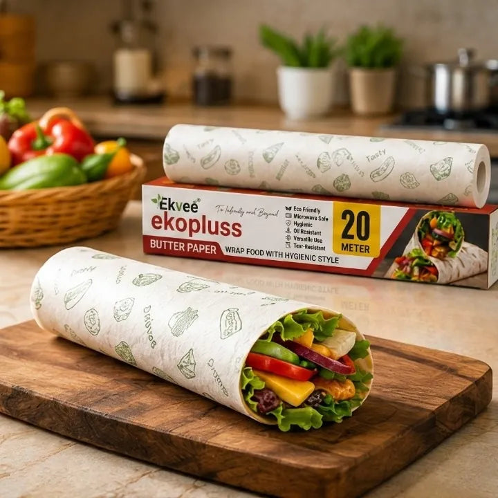 A roll of Ekvee Ekopluss butter paper wrap is shown behind a wrapped sandwich wrap on a wooden cutting board in a kitchen setting. The paper has a light beige background with a green vegetable print, and the roll itself is white with the same pattern.